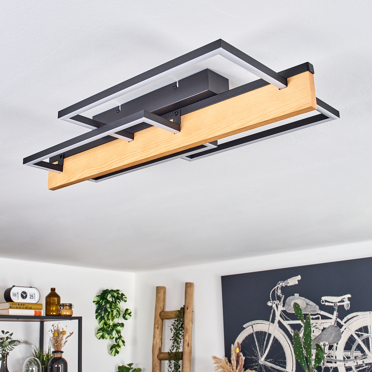 Eine moderne Deckenleuchte mit Holzbalken in der Mitte. Schwarze Metallrahmen umgeben sie. Hintergrund enthält Dekor und Fahrradkunst.