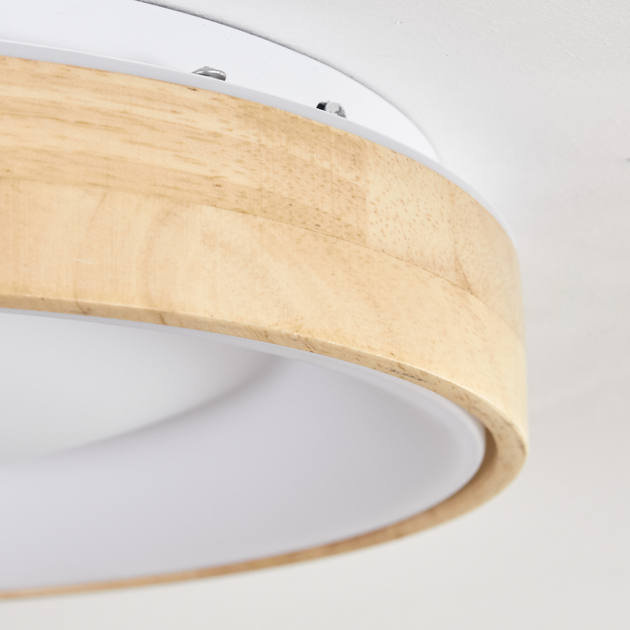 Nahaufnahme einer Deckenleuchte. Sie hat einen Holzring um ein weißes Licht. Der Hintergrund ist eine weiße Decke.
