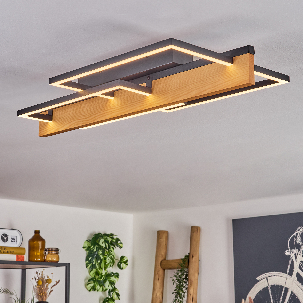 Eine moderne Deckenleuchte mit Holz und schwarzem Metall. Der Raum hat ein Regal, Pflanzen und ein Gemälde eines Fahrrads.
