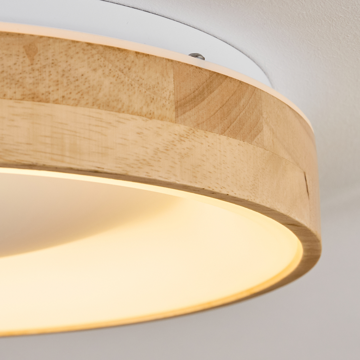 Nahaufnahme einer Deckenlampe. Die Lampe hat einen Holzrahmen und einen weißen Sockel. Das Licht hat eine warme Farbe.