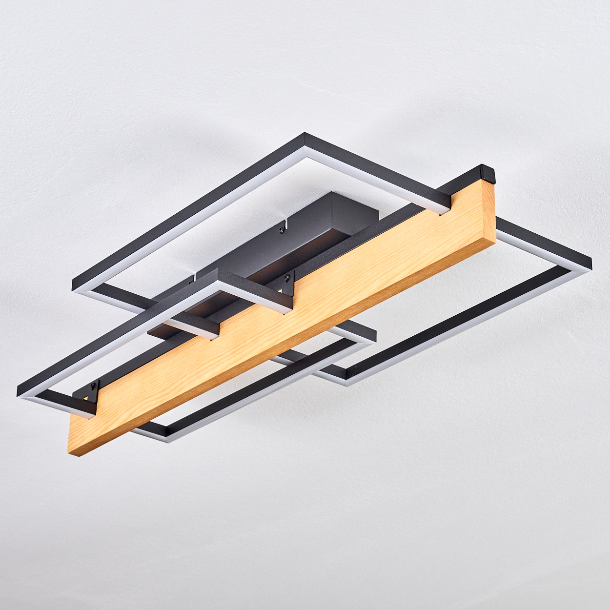 Eine moderne Deckenlampe mit Holzbalken und schwarzen Metallrahmen. Sie ist an einer weißen Decke montiert.