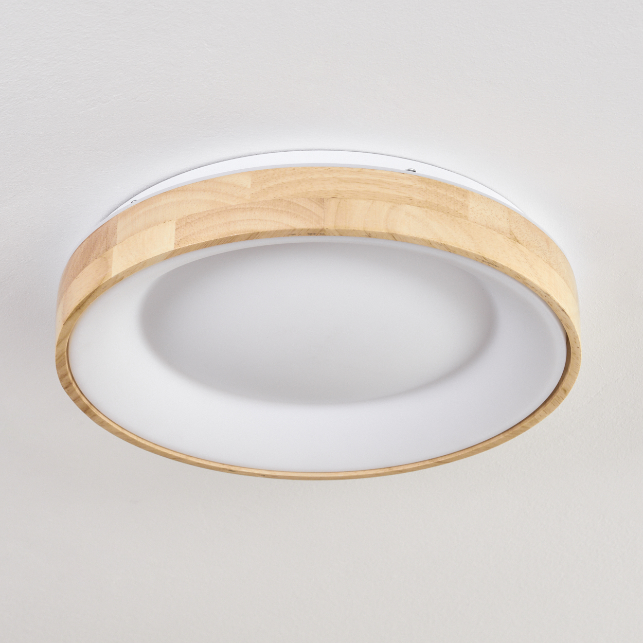 Eine moderne Deckenlampe mit Holzrahmen. Die Lampe hat einen weißen, runden Lichtdiffusor. Der Hintergrund ist eine weiße Decke.