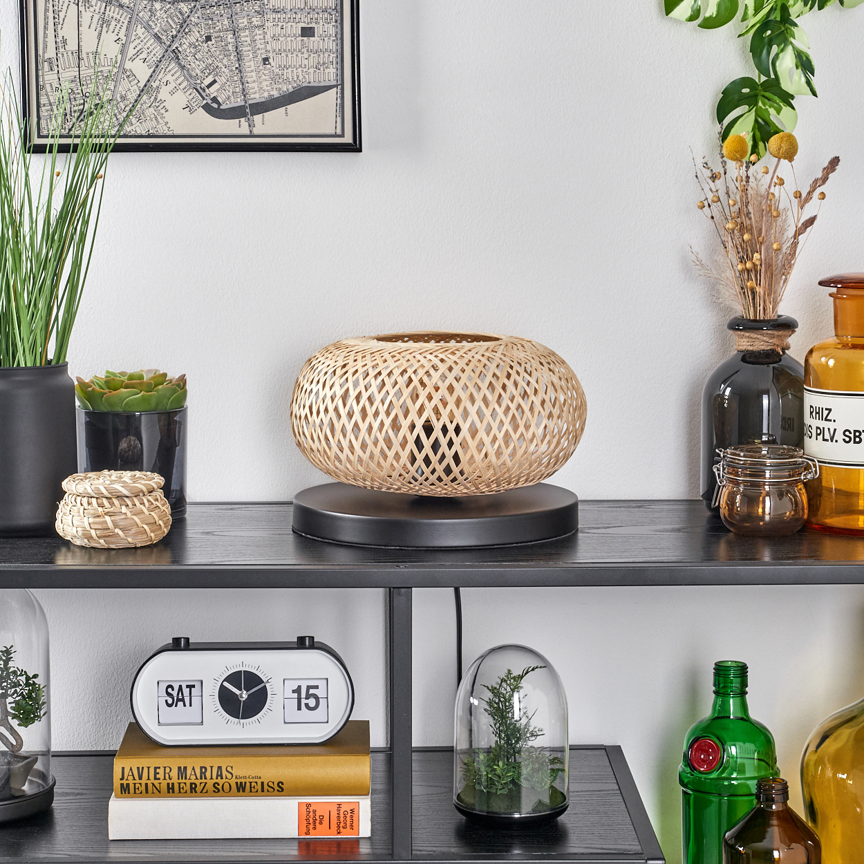 Eine Bambuslampe steht auf einem schwarzen Regal mit Pflanzen, Büchern und anderen Dekorationsgegenständen. Im Hintergrund hängt eine Karte.