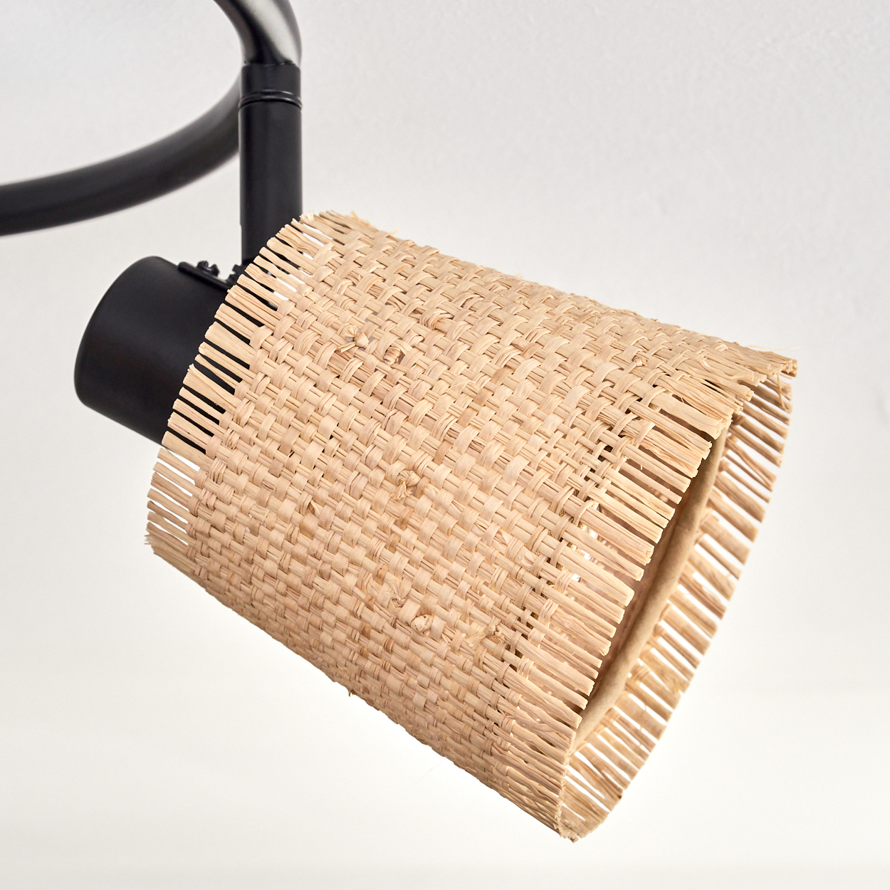 Eine schwarz-beige Lampe. Der Lampenschirm ist zylindrisch und besteht aus gewebtem beigem Material. Die Lampe ist auf einer schwarzen Halterung an einem weißen Hintergrund montiert.