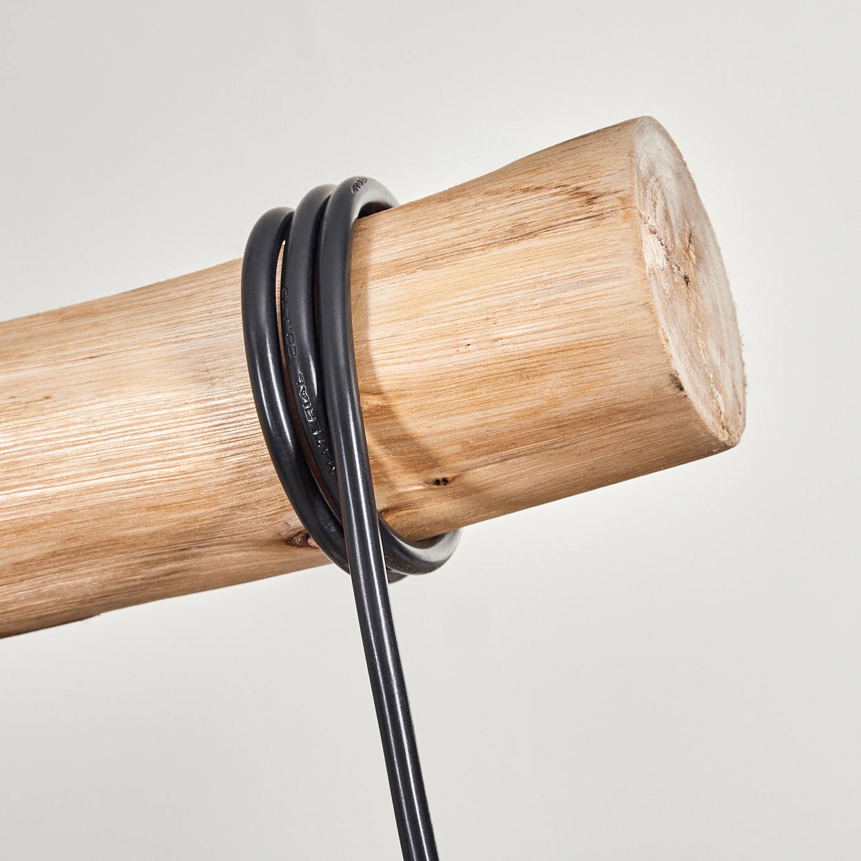 Ein Holzstamm mit einem schwarzen Kabel darum gewickelt. Das Kabel hängt herunter. Der Hintergrund ist schlicht weiß.