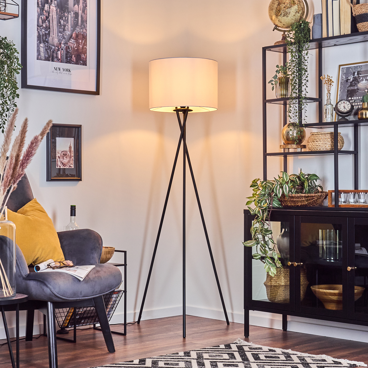 Ein Raum mit einer Stehlampe, einem Stuhl und einem schwarzen Regal mit Dekoration. Ein New York-Poster hängt an der Wand.