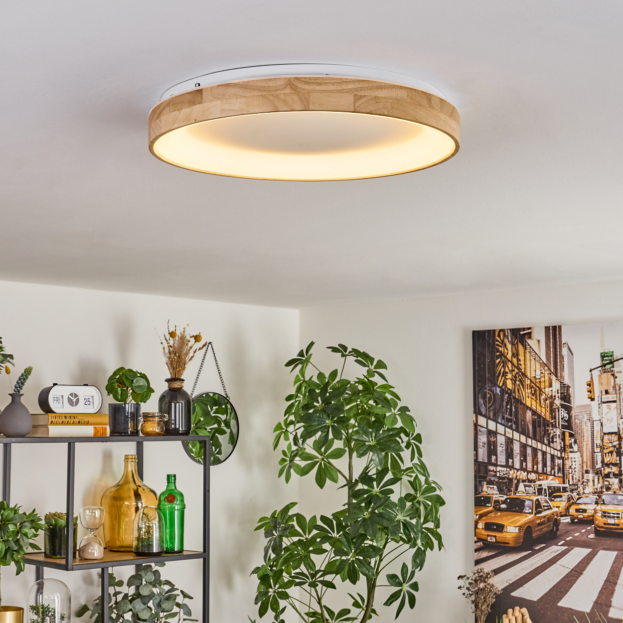 Eine Deckenleuchte mit Holzrahmen leuchtet. Darunter sind eine Pflanze und Dekoration auf einem Regal zu sehen. Ein Gemälde einer NYC-Straßenszene ist an der Wand.