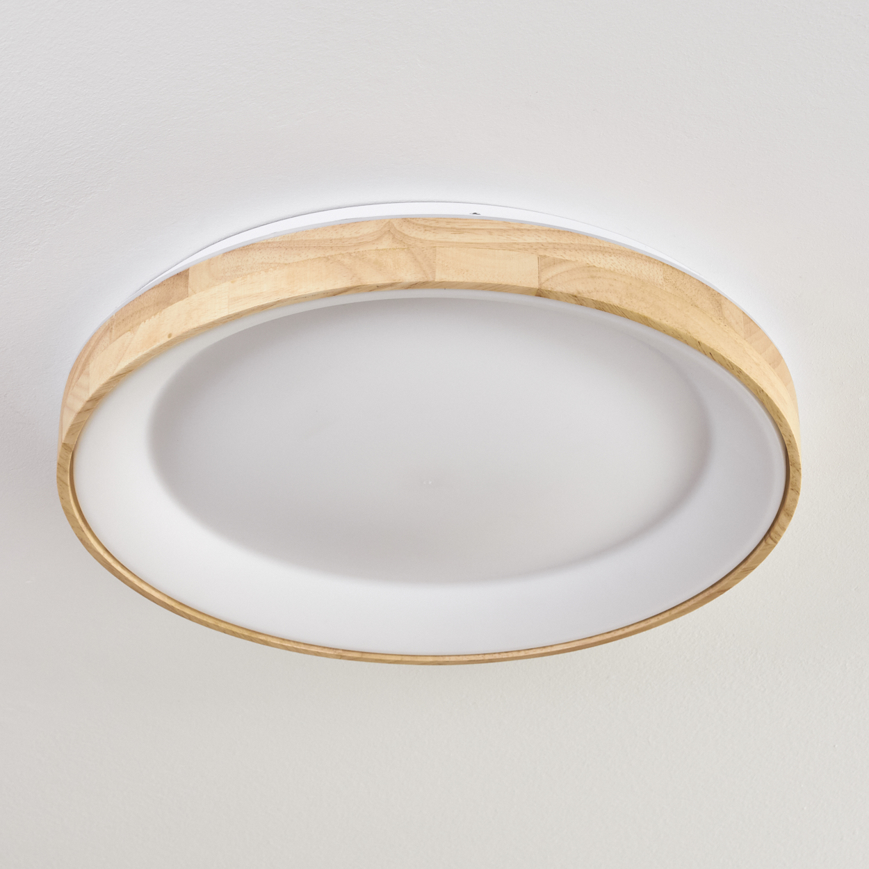 Eine kreisförmige Deckenleuchte mit Holzrahmen und weißer, ovaler Mitte, an einer weißen Decke montiert.