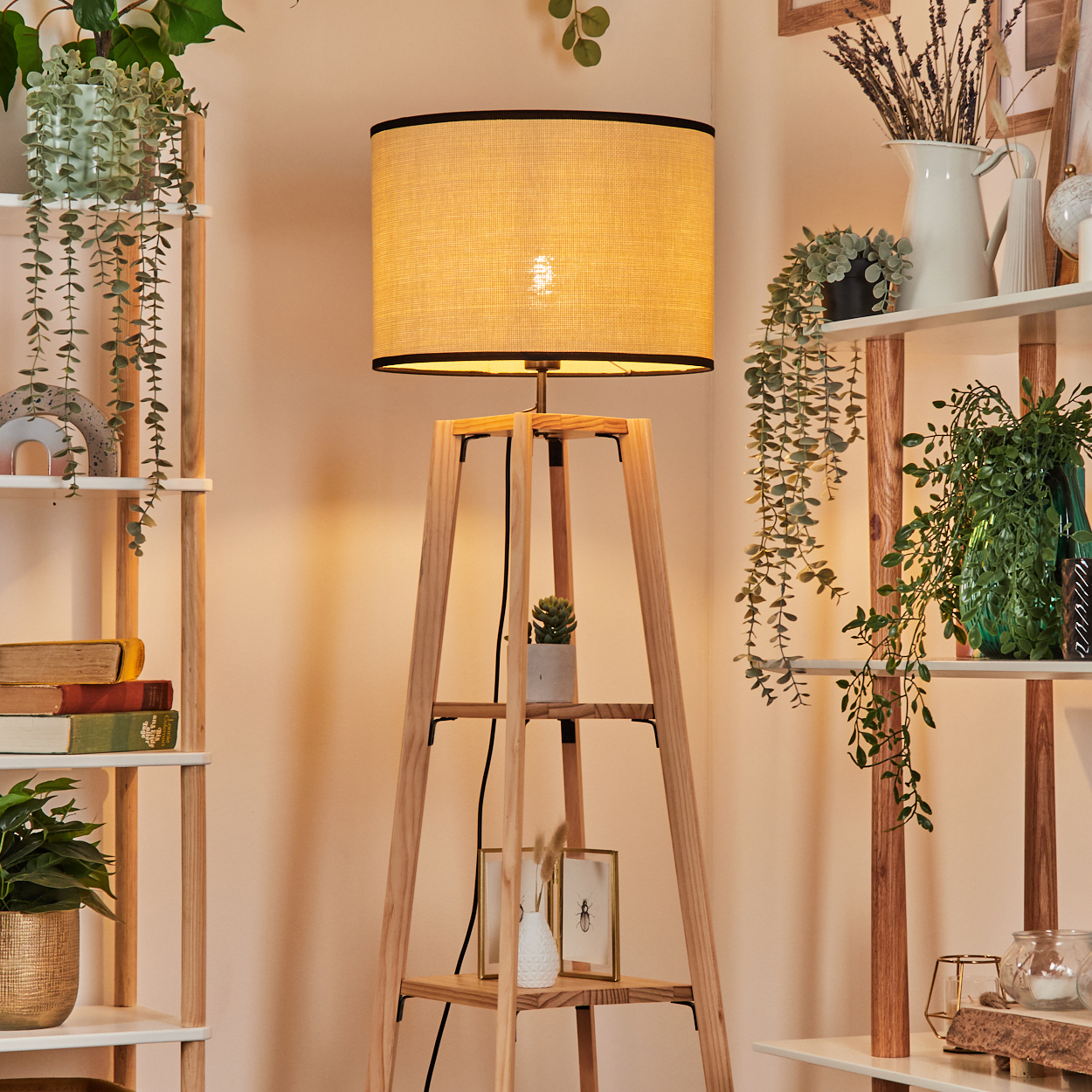 Eine Holzlampe mit beigem Lampenschirm steht in einem Raum mit Regalen voller Pflanzen und Dekorationen.