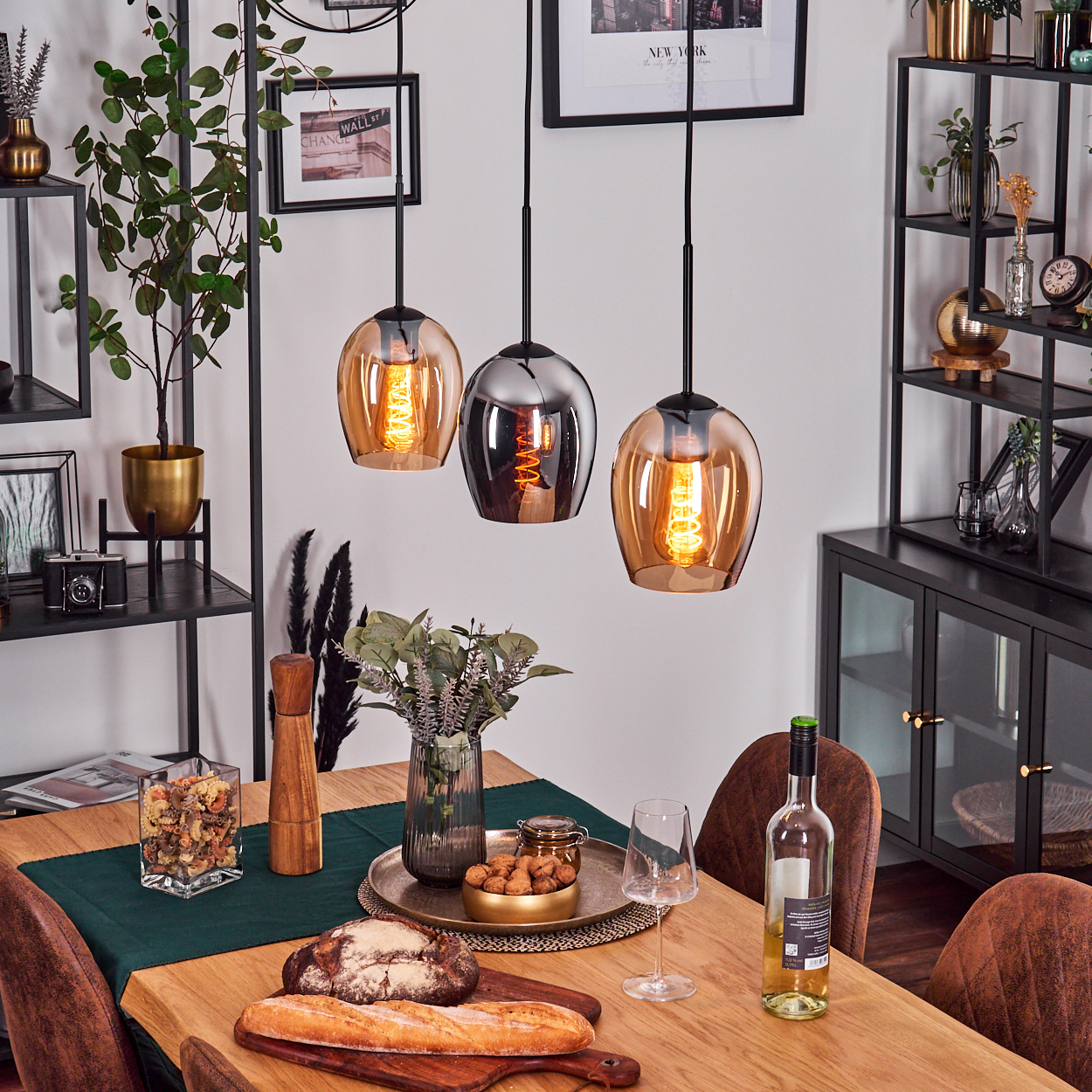 Ein Esszimmer mit Holztisch, Deckenleuchten und Deko. Brot, Wein und eine Blumenvase stehen auf dem Tisch.