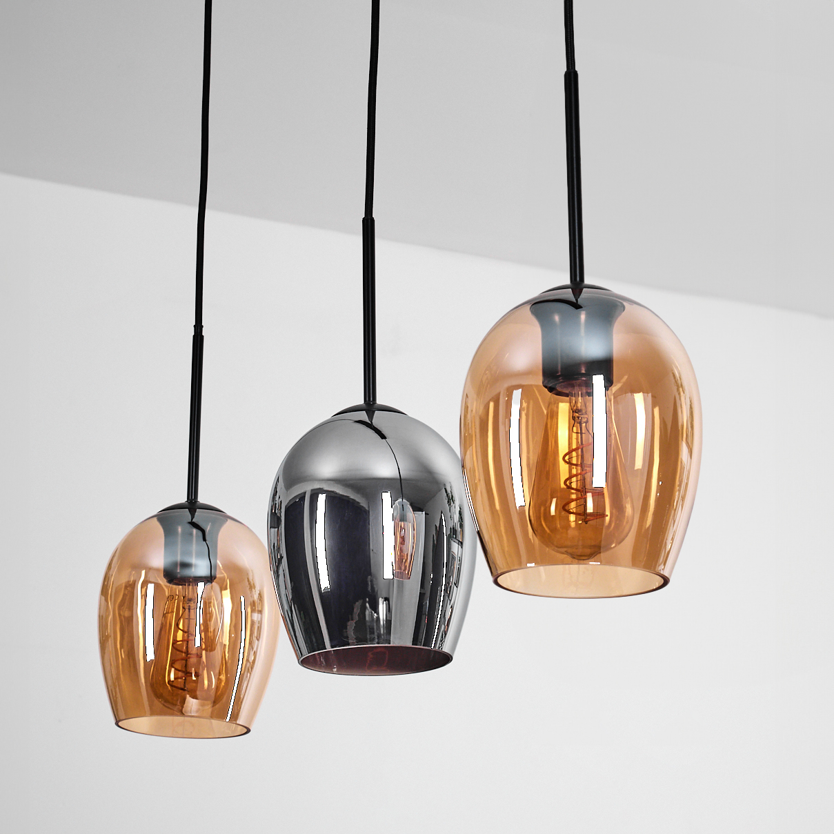 Drei Pendelleuchten mit Glasschirmen in Orange und Silber. Jede hat eine sichtbare Glühbirne, die von einer weißen Decke hängt.
