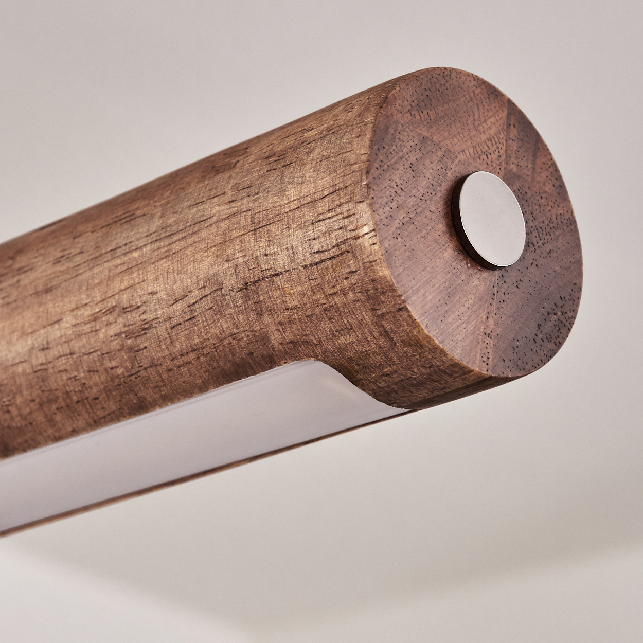Nahaufnahme eines Holz zylinders mit einem weißen Lichtstreifen unten, einem Metallkreis am Ende, vor einem cremefarbenen Hintergrund.