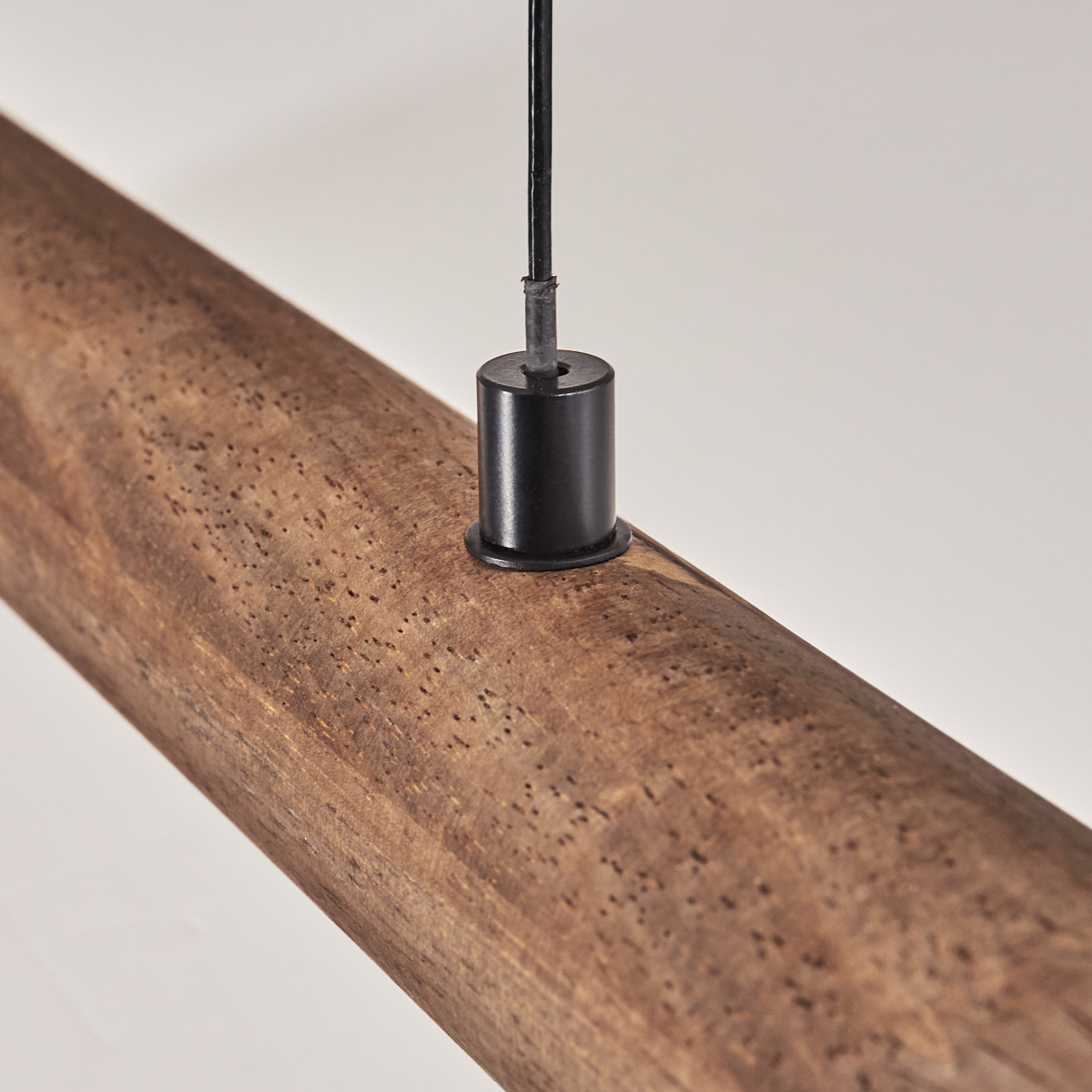 Ein Holzbalken mit einer schwarzen Metallbefestigung und einem Kabel, das von oben hängt. Der Balken ist braun mit kleinen Löchern, vor weißem Hintergrund.