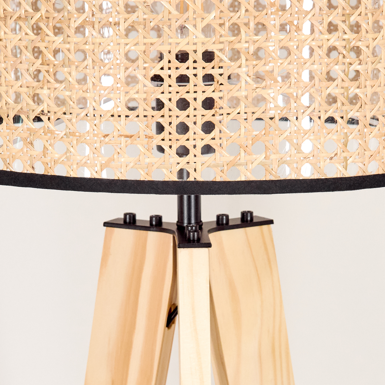 Nahaufnahme einer Lampe. Der Lampenschirm ist hellbraun gewebt. Der Sockel ist helles Holz mit schwarzem Metall. Der Hintergrund ist weiß.