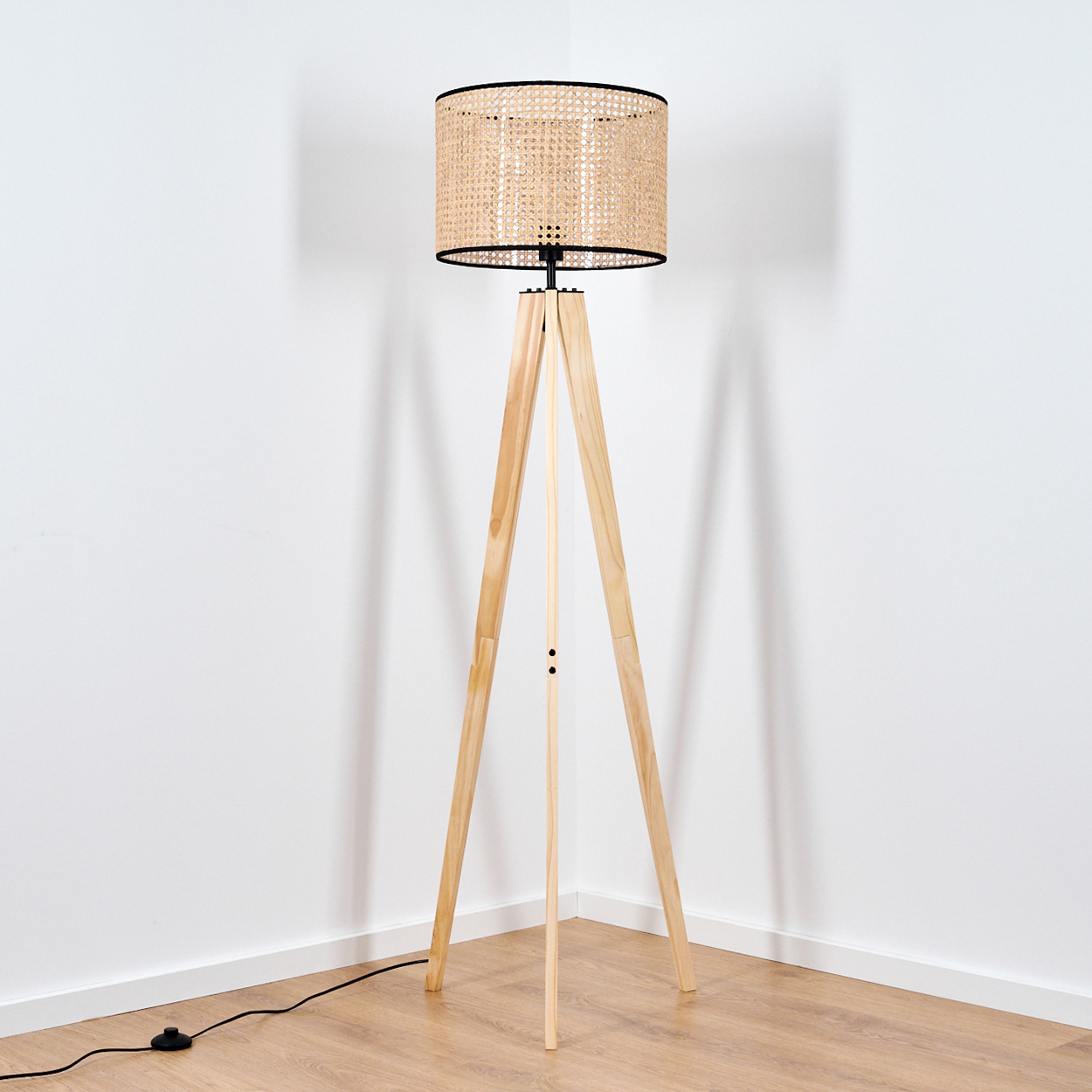 Eine Stehlampe aus Holz mit einem Lampenschirm aus Weide steht vor einer weißen Wand auf einem Holzboden.