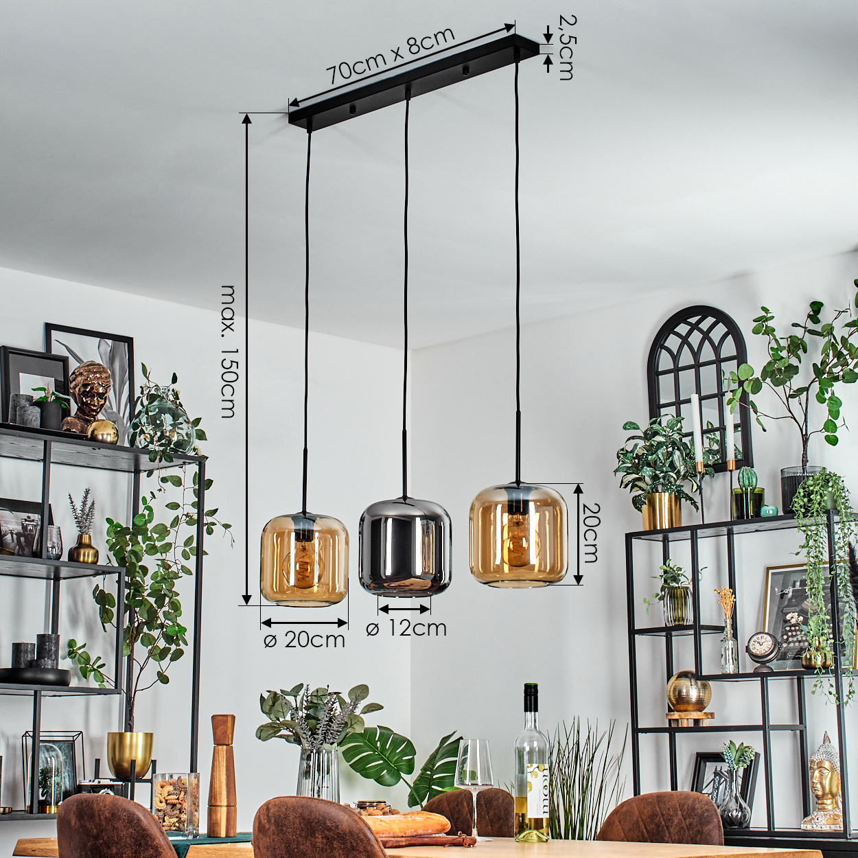 Drei Pendelleuchten mit bernsteinfarbenen Glasschirmen hängen über einem Holztisch. Im Hintergrund Regale mit Pflanzen und Dekor.