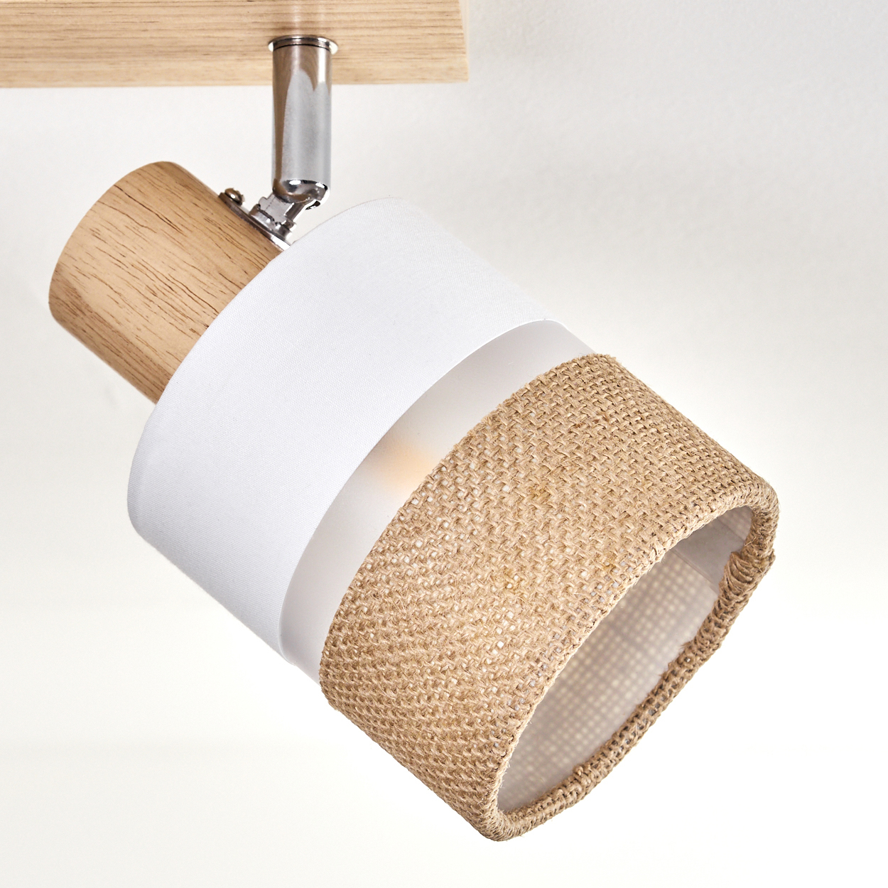 Ein Strahler ist an einem Holzbalken befestigt. Er hat ein weißes Stoffband, einen gewebten Juteabschnitt und einen Holzsockel.