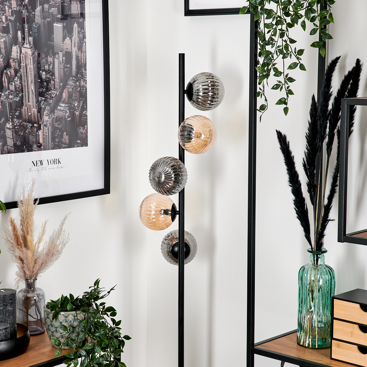 Eine Stehlampe mit Glaskugeln, ein New York-Bild, Pflanzen in Vasen und ein Holzregal.