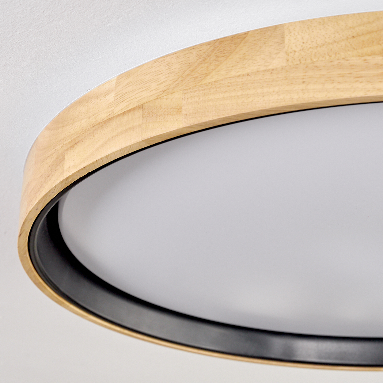 Nahaufnahme einer kreisförmigen Deckenleuchte. Sie hat einen Holzrahmen, einen schwarzen Ring und eine weiße, undurchsichtige Lichtplatte.