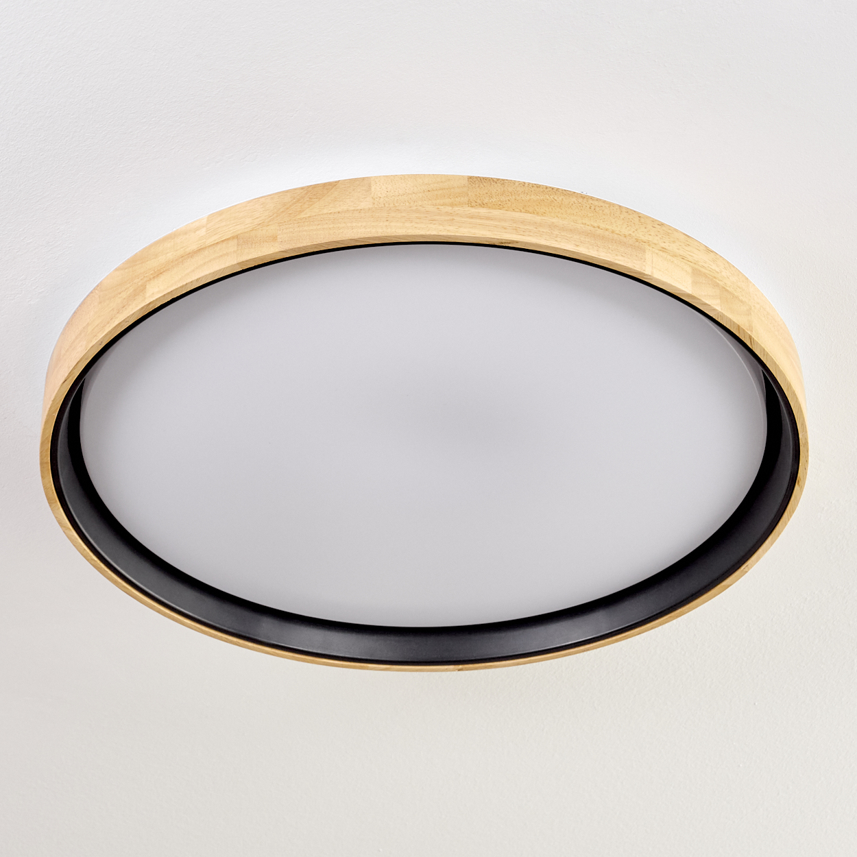 Eine kreisförmige Deckenleuchte. Sie hat einen Holzrahmen, einen schwarzen Innenring und einen weißen Lichtdiffusor.