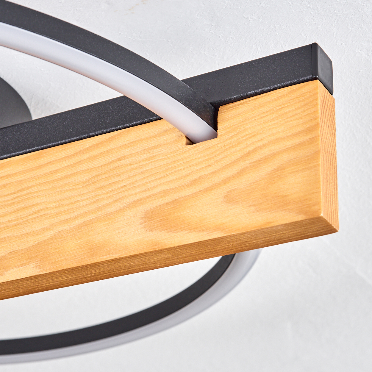 Nahaufnahme einer modernen Leuchte. Merkmale: Holzbalken, schwarze Metallakzente und ein weißes, gebogenes Leuchtelement. Der Hintergrund ist weiß.