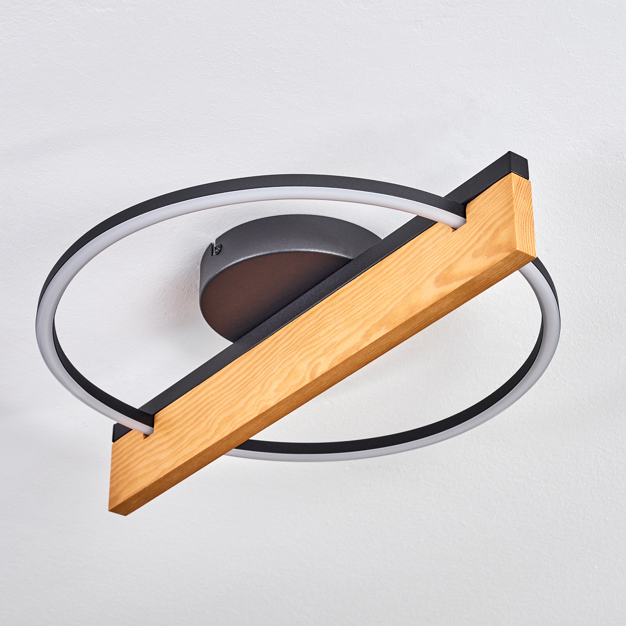 Deckenlampe mit Holzbalken und kreisförmigem Licht. Die Lampe hat einen schwarzen Rahmen und ist an einer weißen Decke befestigt.