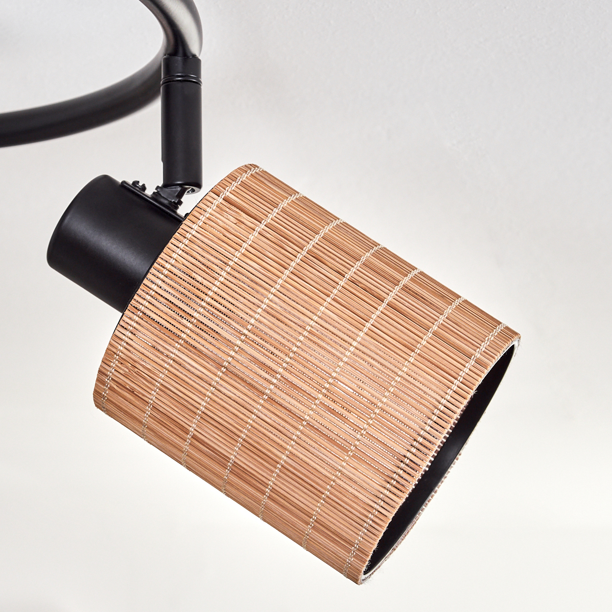 Eine Deckenlampe mit Bambus-Lampenschirm. Die Lampe hat einen schwarzen Metallkörper und einen hellbraunen, zylindrischen Lampenschirm.