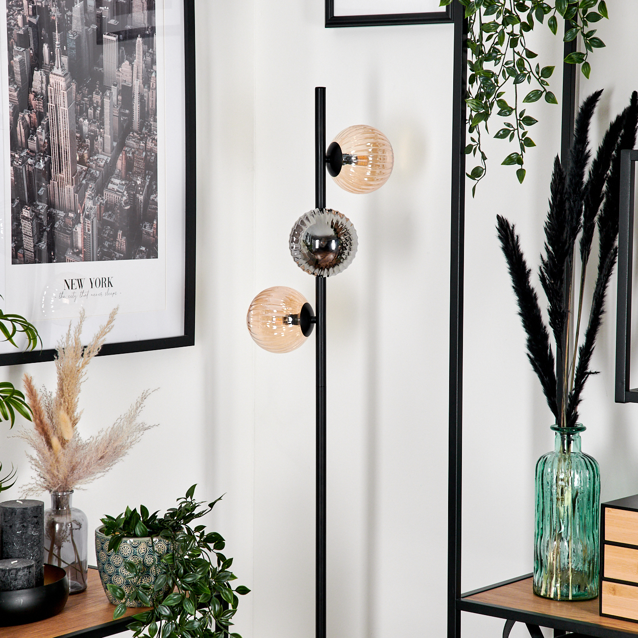 Eine moderne Lampe mit drei Kugelleuchten. Ein New York-Stadtbilddruck, Pflanzen und dekorative Vasen im Hintergrund.