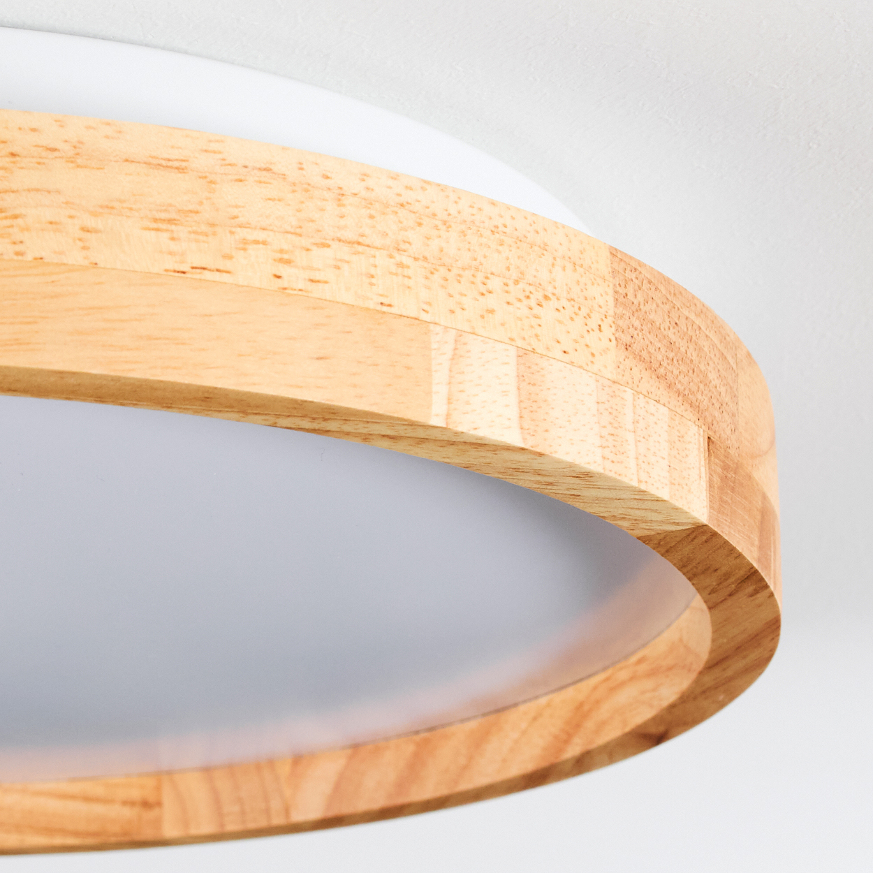 Nahaufnahme einer Deckenleuchte mit Holzrahmen und weißem Diffusor. Der Holzrahmen ist gebogen und der Hintergrund ist weiß.