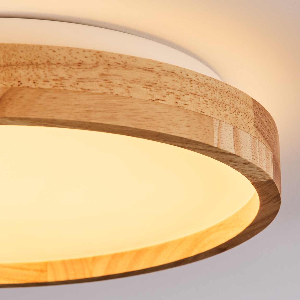 Nahaufnahme einer Deckenleuchte. Sie hat einen Holzring um eine weiße Basis. Das Licht ist an und leuchtet.