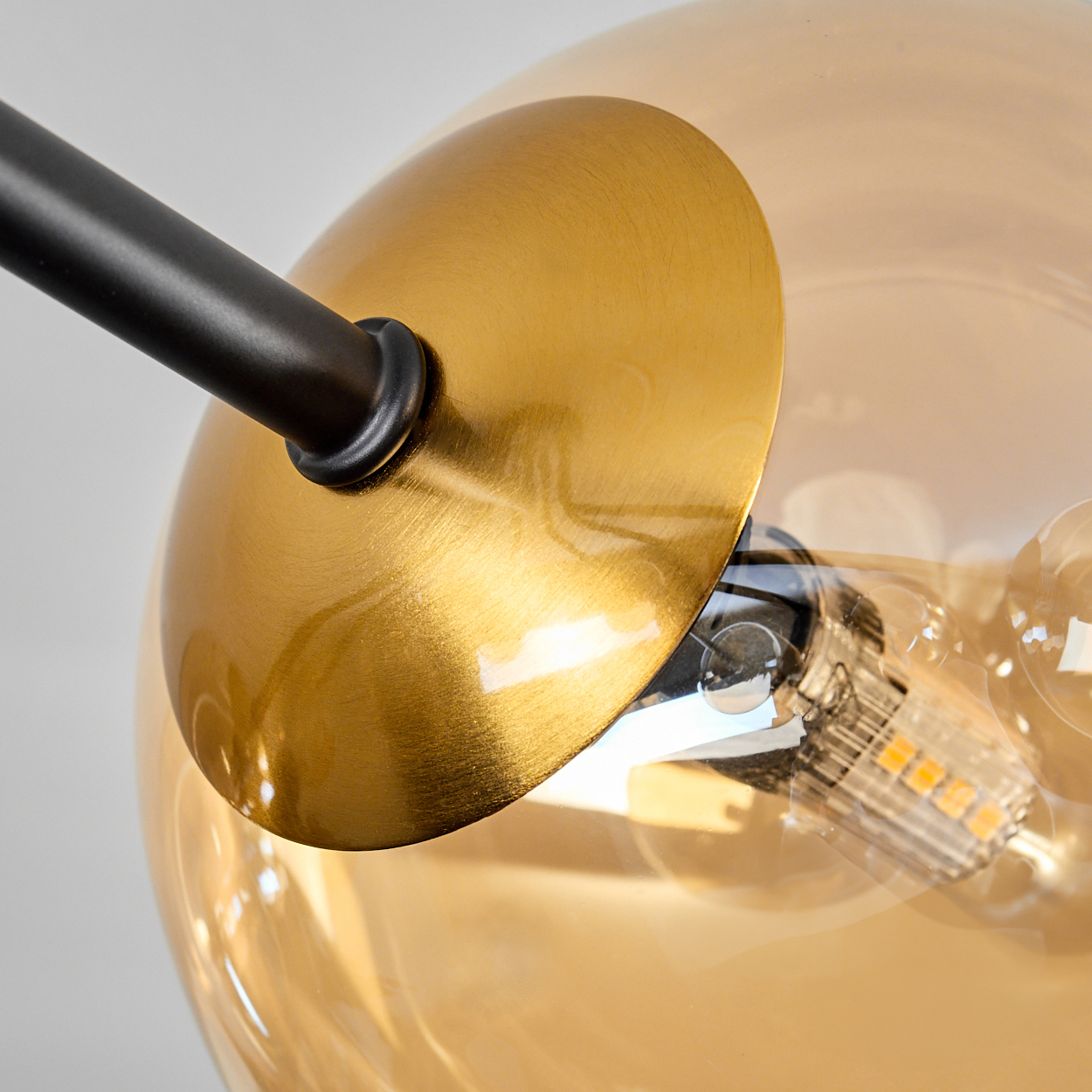 Nahaufnahme einer modernen Lampe. Sie hat eine goldene Kuppel, einen schwarzen Stiel und eine Glaskugel mit einer sichtbaren Glühbirne.