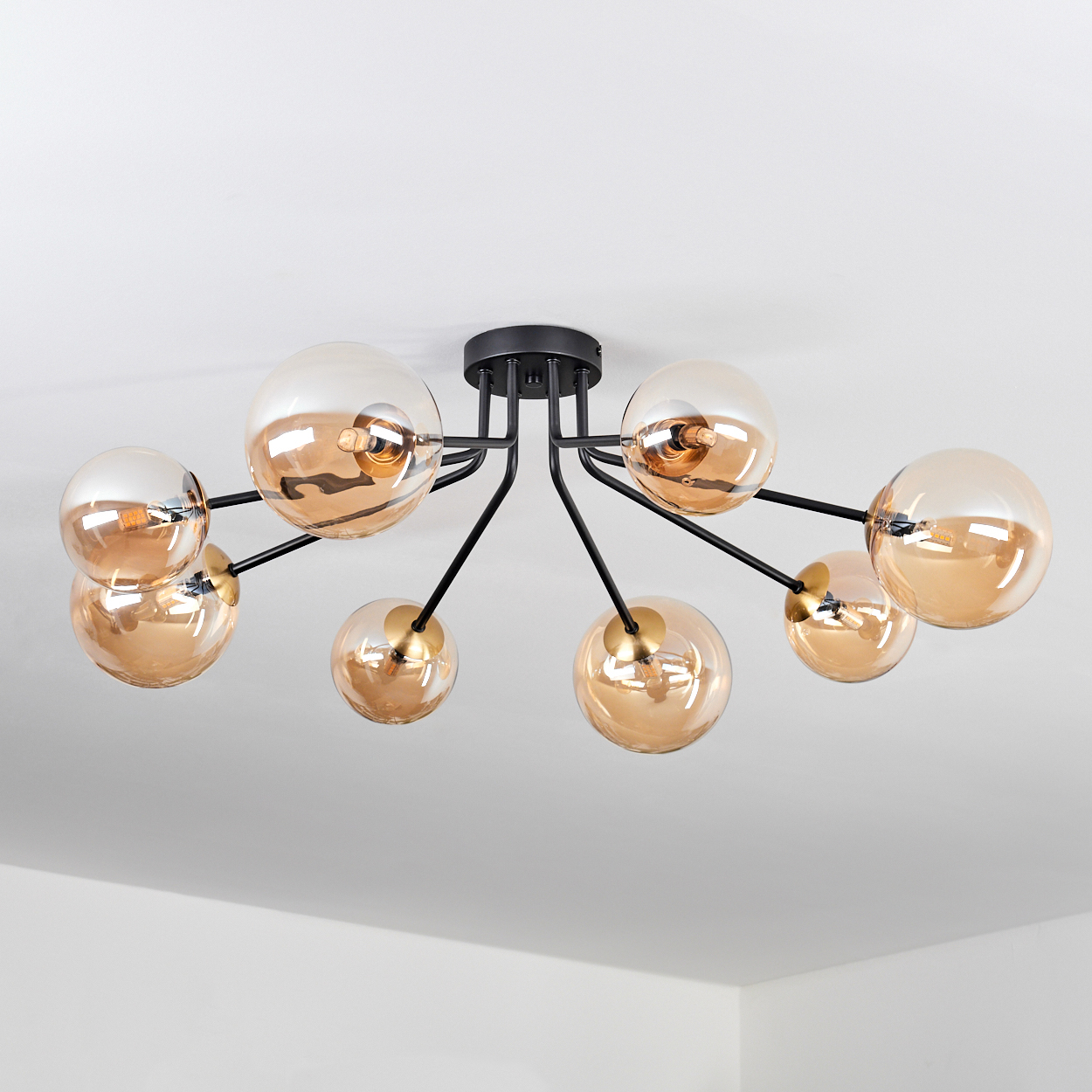 Eine schwarze Deckenlampe mit acht bernsteinfarbenen Glaskugeln und einem weißen Deckenhintergrund. Jede Kugel hat eine sichtbare Glühbirne.