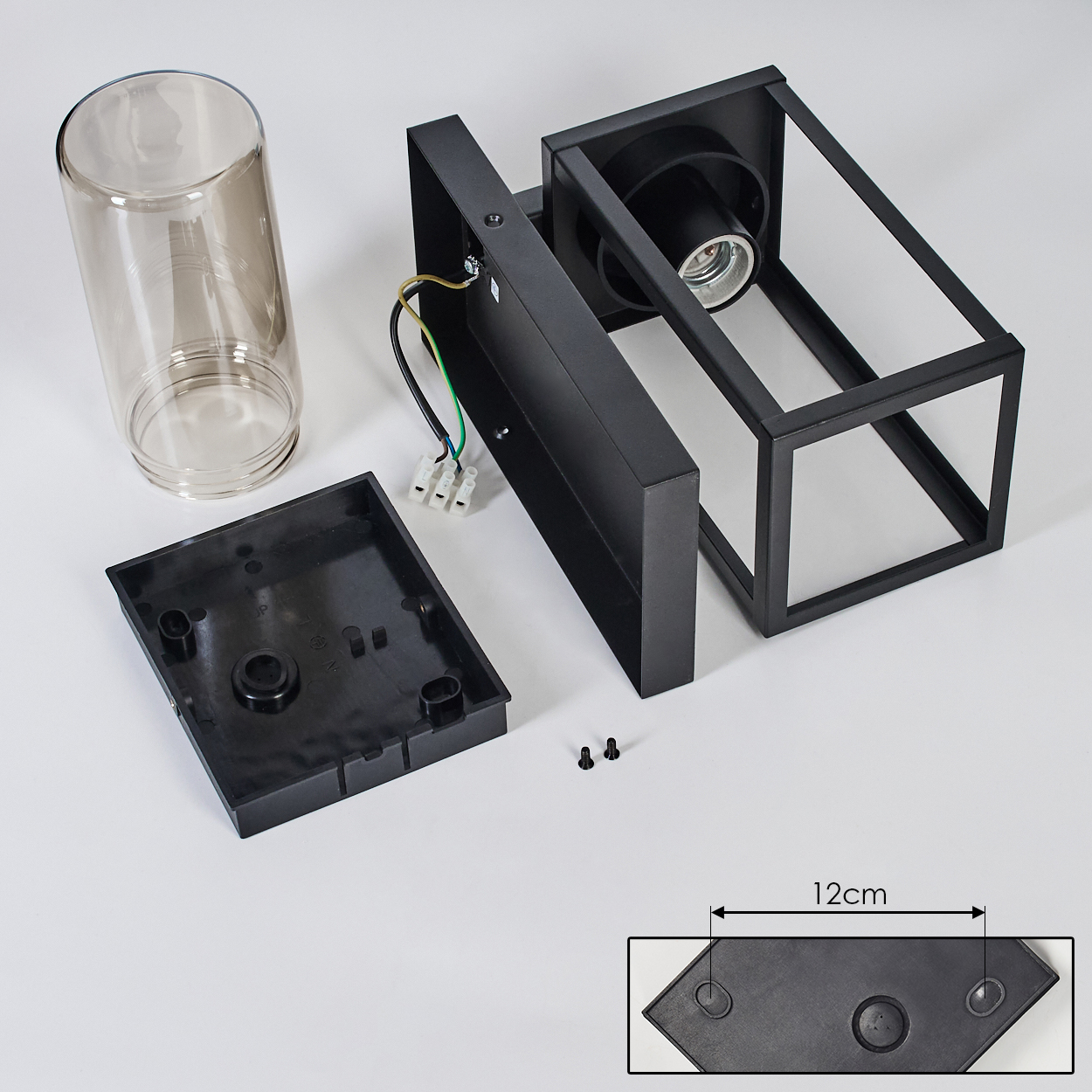 Zerlegte schwarze Außenlampe mit Glaszylinder und Sockel. Teile: Rahmen, Sockel, Schrauben und Verkabelung, alles auf weißer Oberfläche.