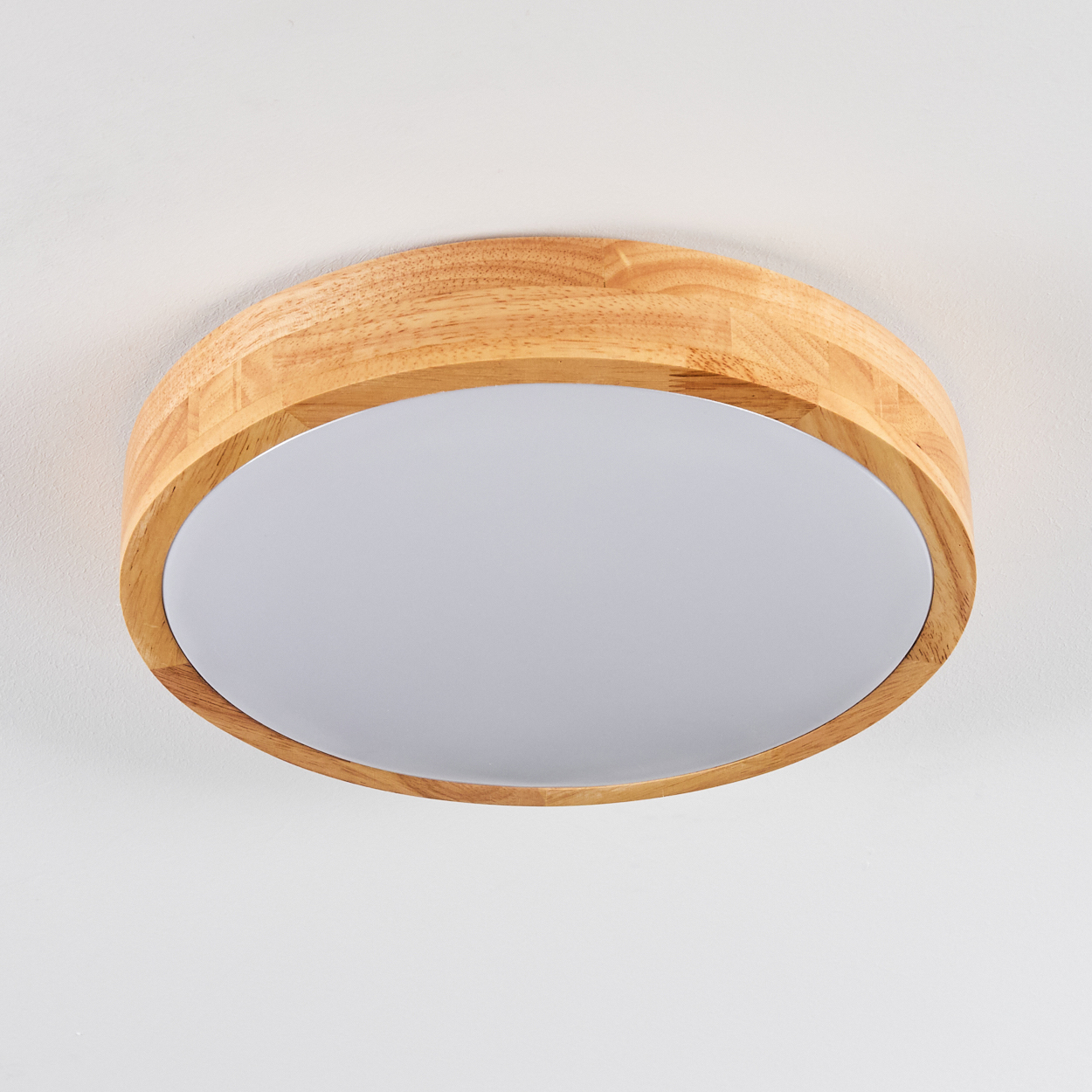 Eine runde Deckenleuchte aus Holz mit einem weißen, durchscheinenden Mittelteil. Das Licht ist vor weißem Hintergrund zentriert.