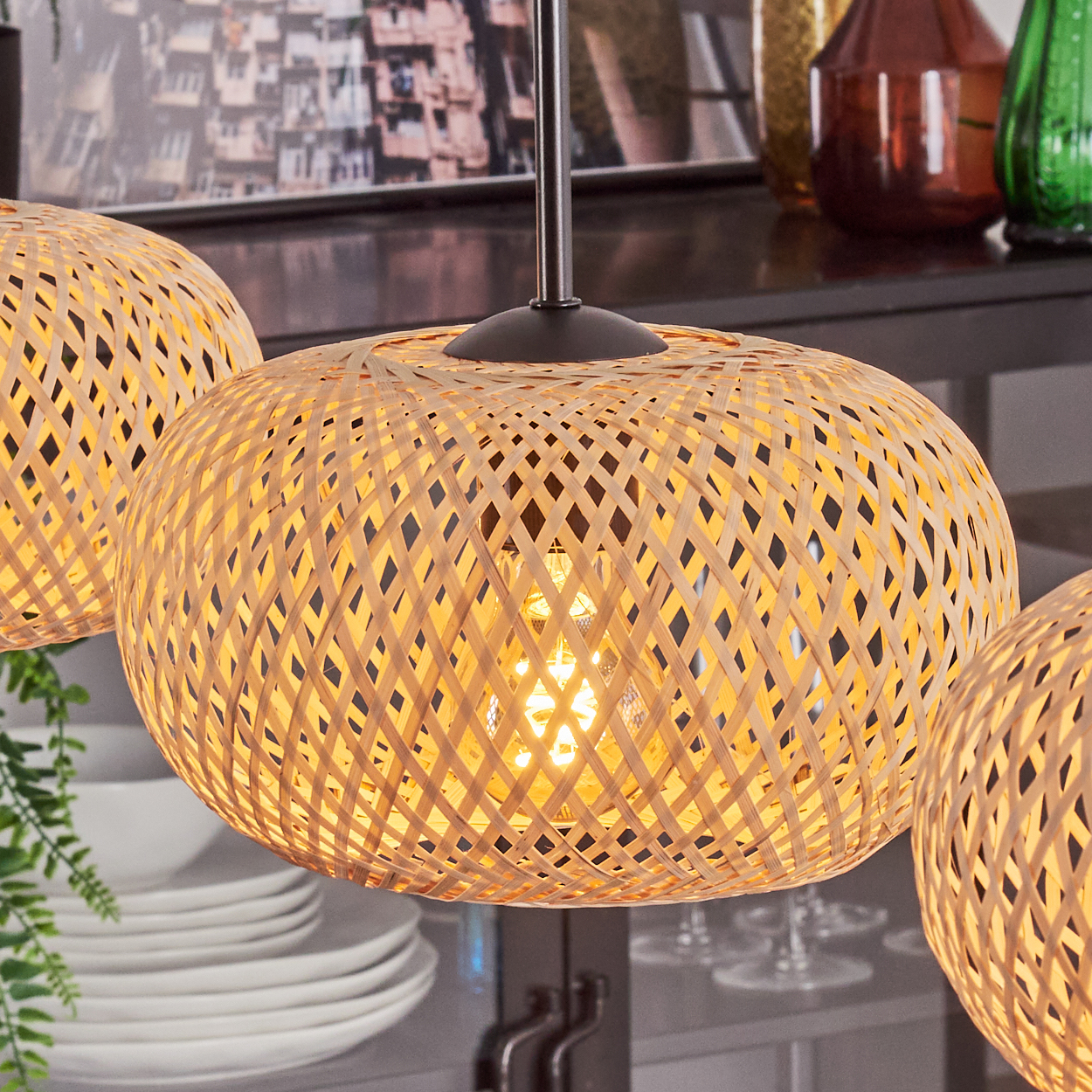 Drei gewebte Lampen hängen von der Decke. Die Lampen sind beleuchtet und beleuchten die gewebten Muster. Der Hintergrund umfasst Geschirr und Dekor.