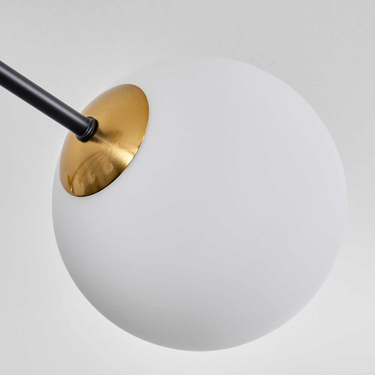 Nahaufnahme einer weißen Kugelleuchte mit schwarzem Arm und goldenem Akzent. Der Hintergrund ist schlicht weiß.