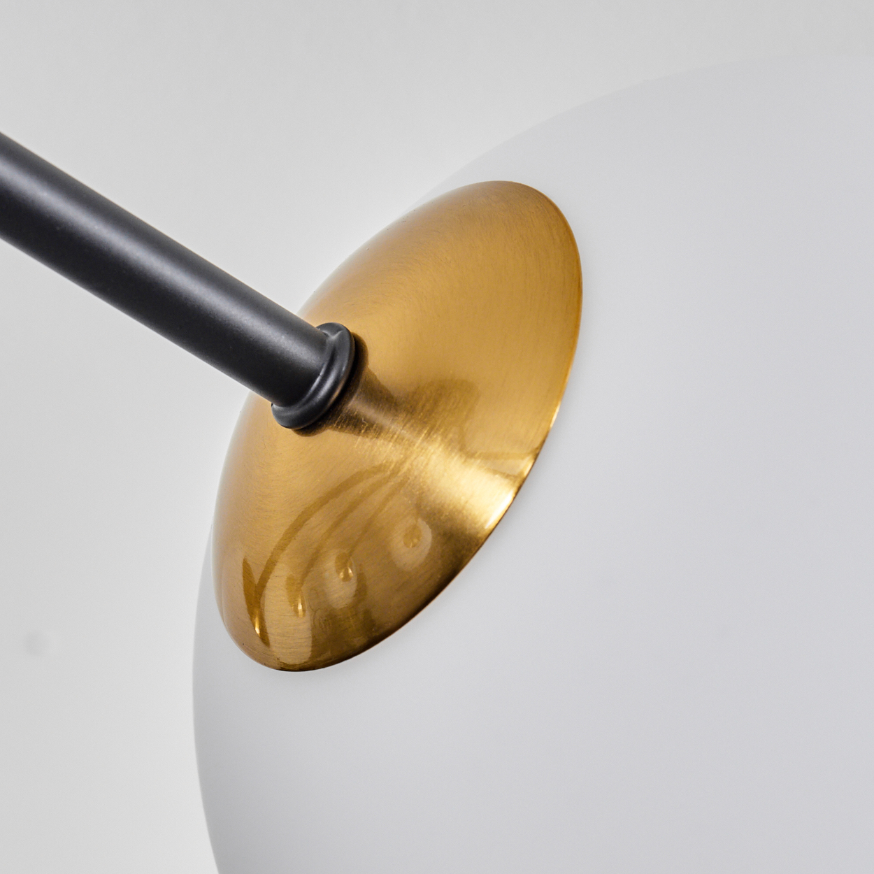 Nahaufnahme einer modernen Lampe. Sie hat einen schwarzen Arm, einen goldfarbenen Schirm und einen weißen, abgerundeten Diffusor. Der Hintergrund ist weiß.