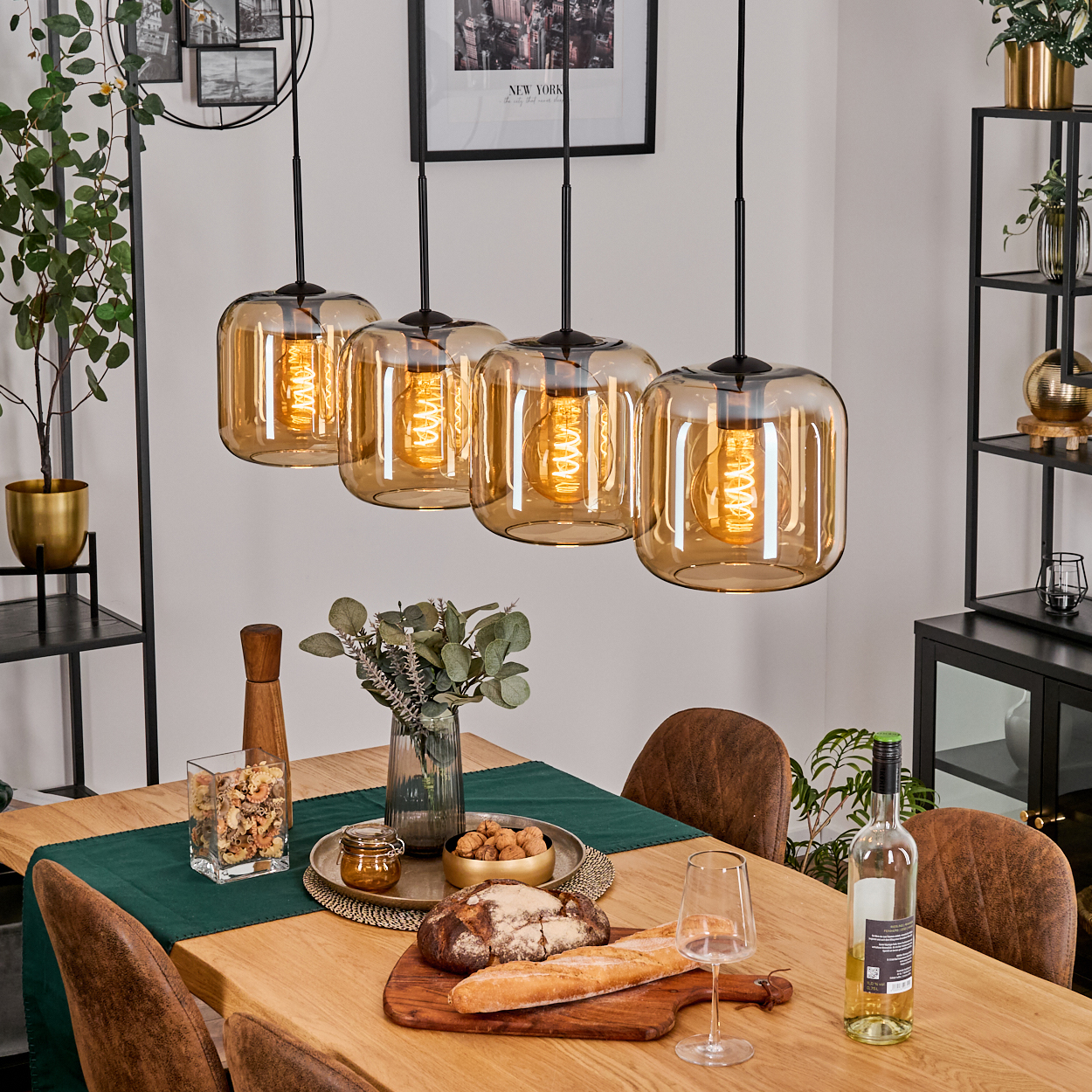 Esszimmer-Szene mit bernsteinfarbenen Pendelleuchten, Tisch mit Essen und Wein, und einem schwarzen Regal. Ein Bild hängt an der Wand.