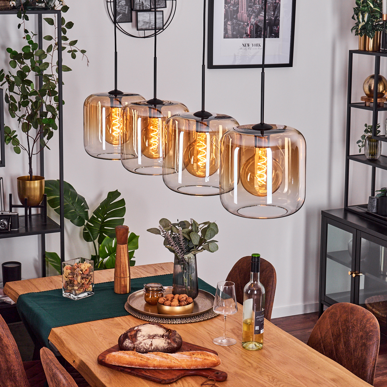 Esszimmer mit Holztisch, Glaslampen, Essen, Wein und Stühlen. Regale mit Pflanzen und Dekoration im Hintergrund.