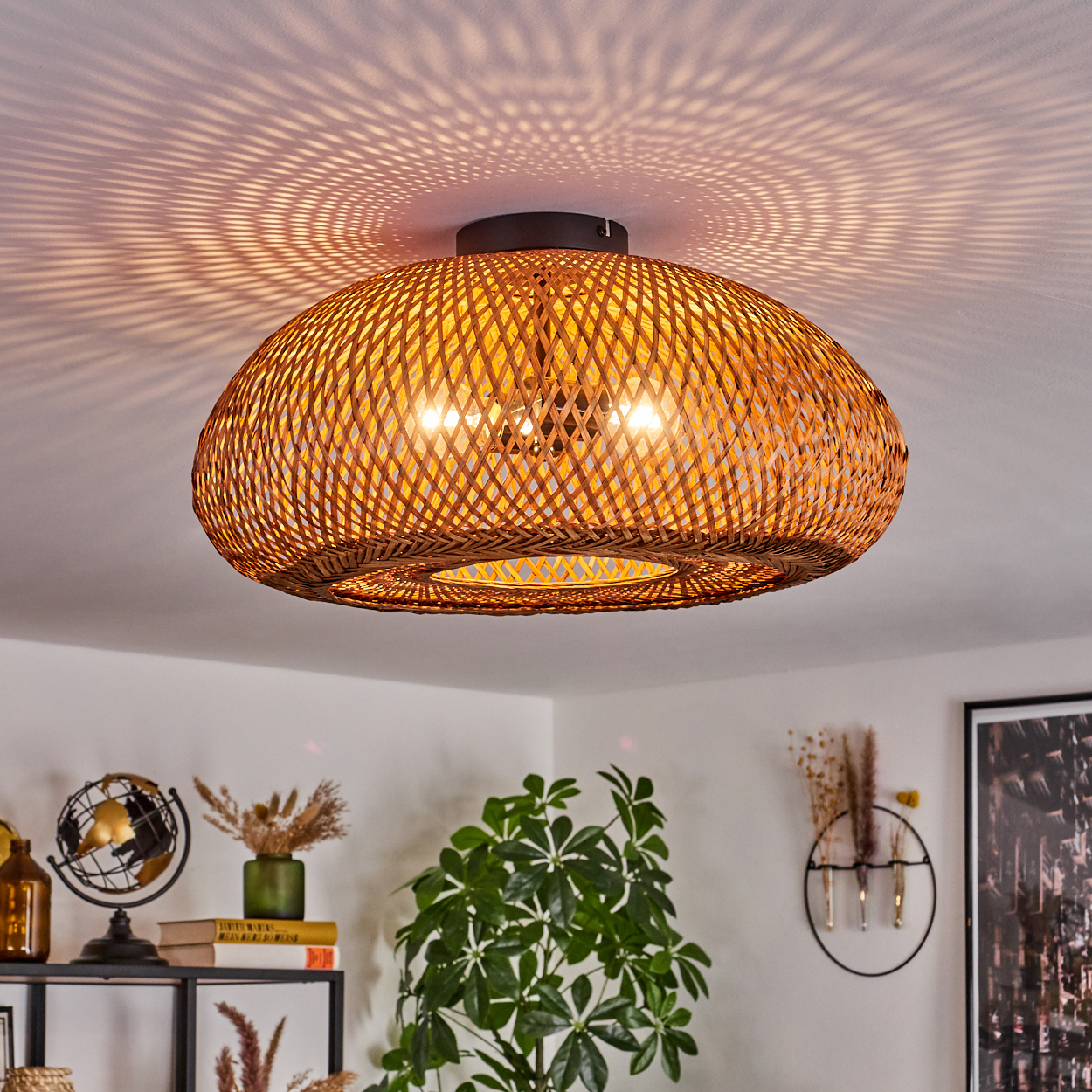 Geflochtene Deckenlampe aus Rattan, wirft Musterlicht. Darunter Pflanzen und Dekorationen auf Regalen.