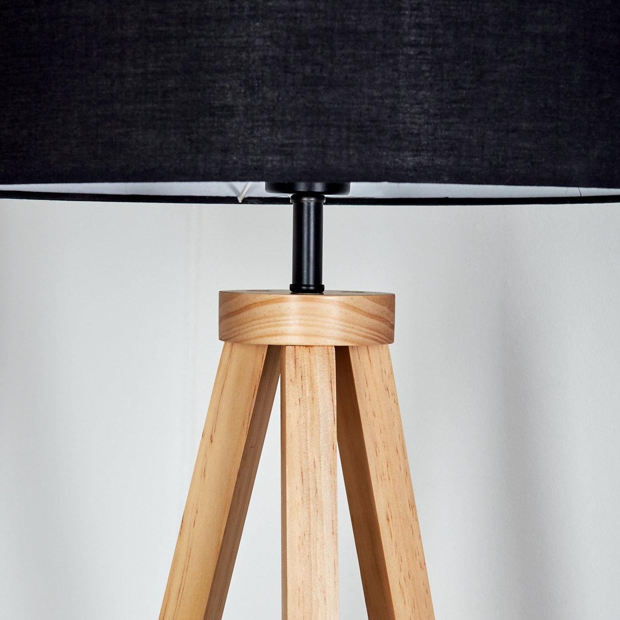 Nahaufnahme einer Holz-Stativlampe. Sie hat einen schwarzen Lampenschirm und eine schwarze Metallhalterung. Der Hintergrund ist weiß.