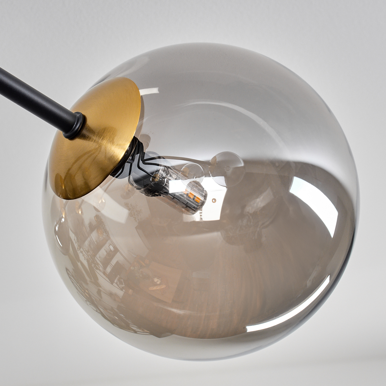 Nahaufnahme einer modernen Lampe. Sie hat eine große, rauchige Glaskugel mit einer Glühbirne. Die Leuchte hat goldene und schwarze Akzente.