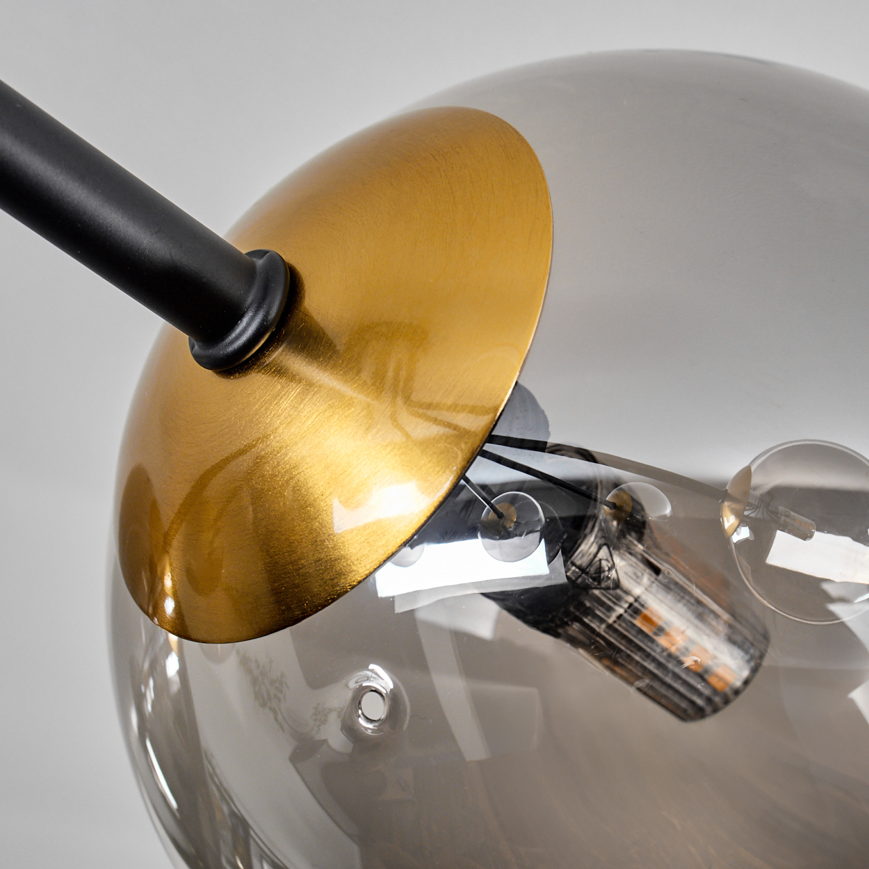 Nahaufnahme einer modernen Lampe. Sie hat einen goldfarbenen Metallschirm und eine klare, rauchige Glaskugel. Schwarzer Arm.