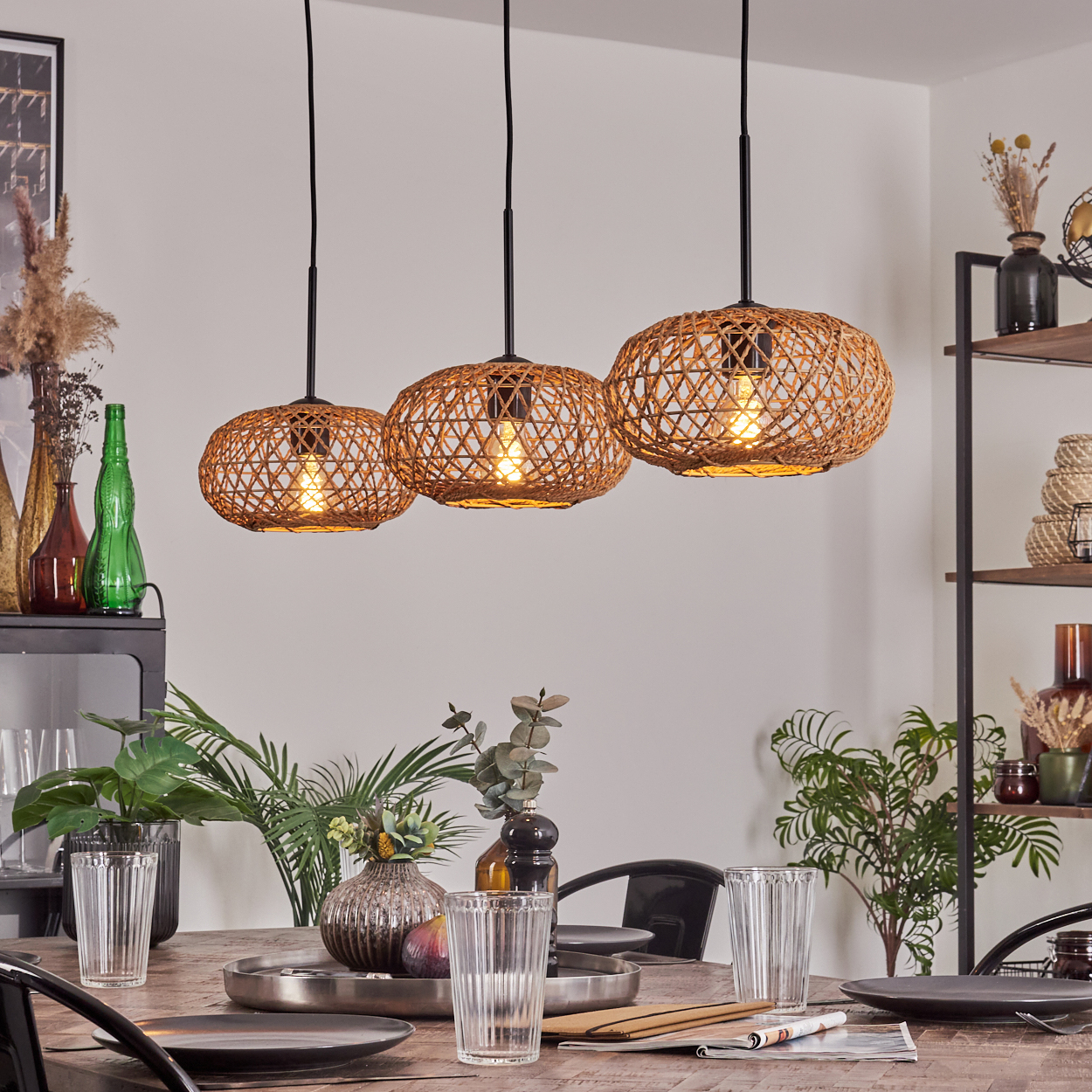 Drei gewebte Pendelleuchten hängen über einem Holztisch. Der Tisch ist mit Tellern, Gläsern und Dekorationsartikeln gedeckt.