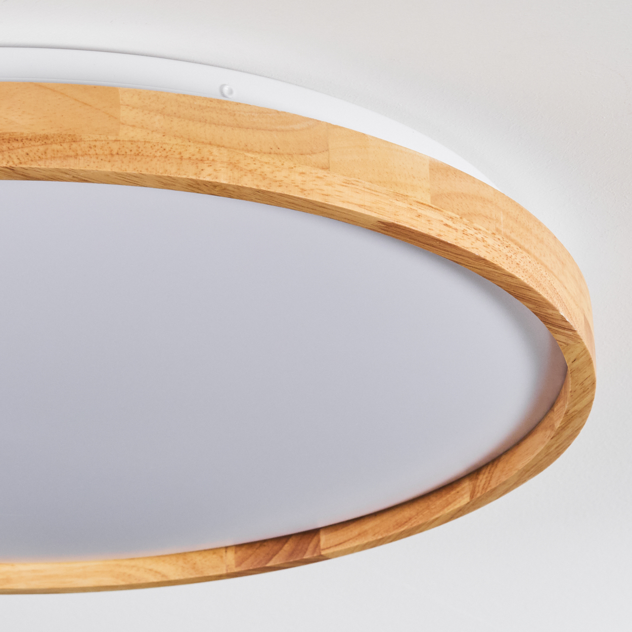 Nahaufnahme einer modernen Deckenlampe. Sie hat einen Holzrahmen, einen weißen Sockel und eine lichtemittierende Oberfläche. Der Hintergrund ist eine weiße Decke.