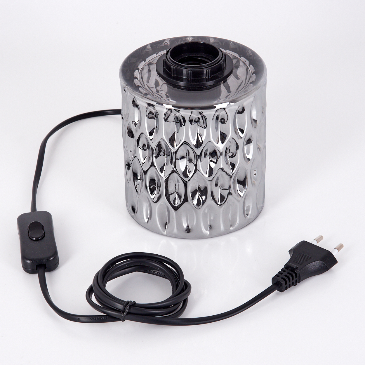 Eine silberne Lampe mit schwarzem Sockel, Schalter und Stecker. Die Lampe hat eine gemusterte Oberfläche. Ein schwarzes Kabel verbindet sie.