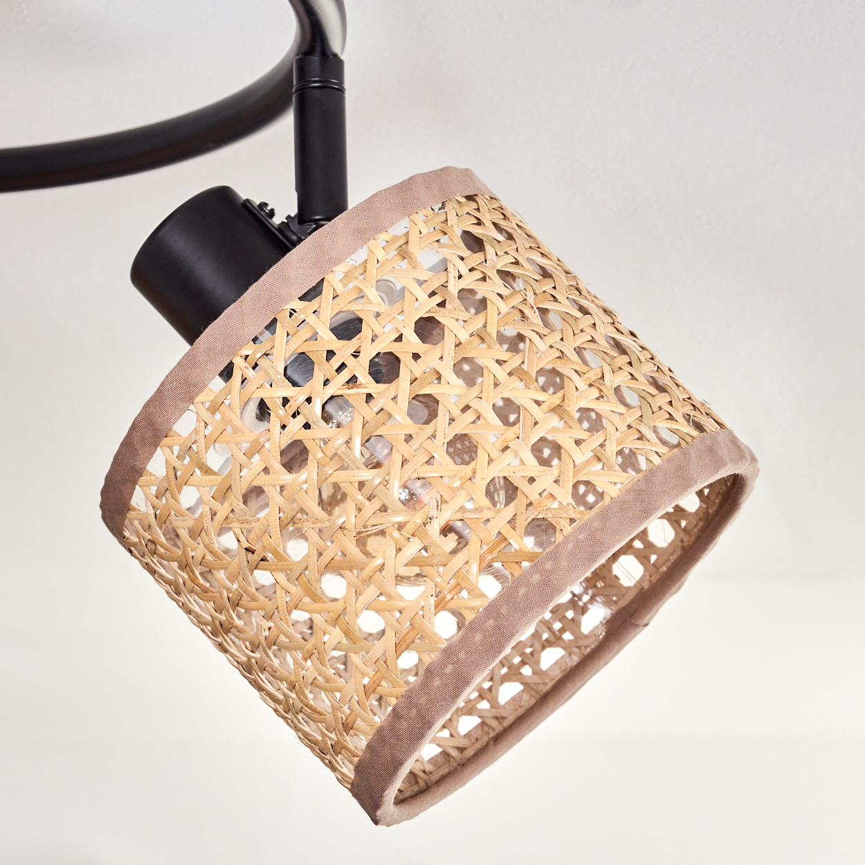 Ein Lampenschirm aus Rattan mit schwarzer Halterung. Der Lampenschirm ist beige und hat eine braune Einfassung. Der Hintergrund ist weiß.