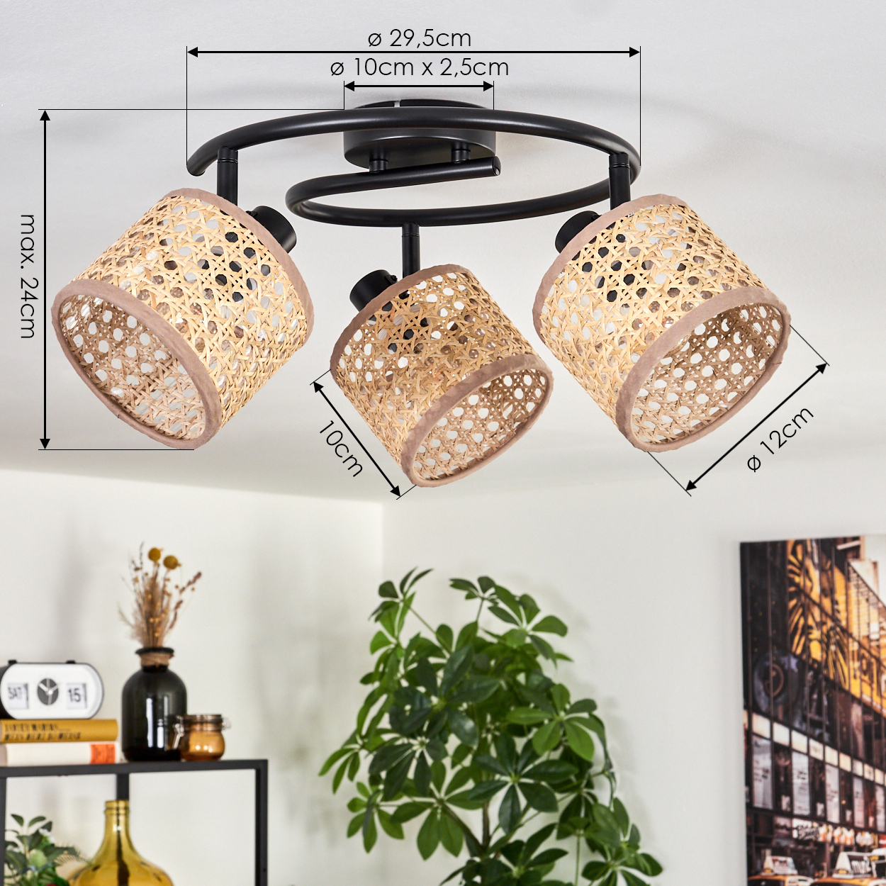 Eine Deckenlampe mit drei Korblampenschirmen, braunen Rändern und einem schwarzen Rahmen. Abmessungen sind angegeben. Eine Pflanze und Deko im Hintergrund.
