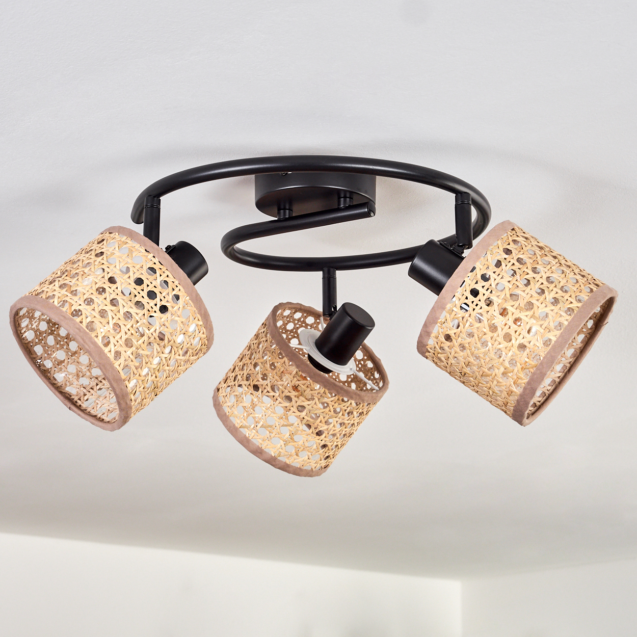 Eine Deckenlampe mit drei gewebten Lampenschirmen. Der Metallrahmen ist schwarz. Die Lampenschirme sind beige mit braunem Rand und zylindrisch.