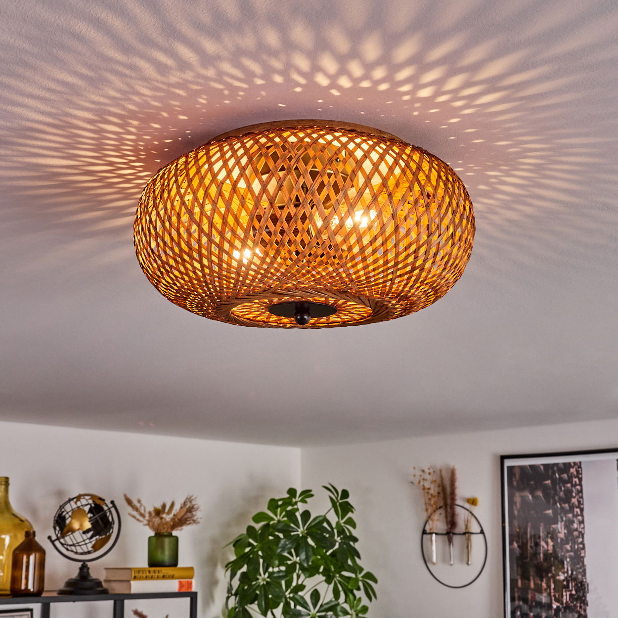 Eine Deckenlampe aus Korbgeflecht ist der Mittelpunkt. Sie wirft gemustertes Licht auf die Decke. Darunter ein Raum mit Pflanzen und Dekorationsartikeln.